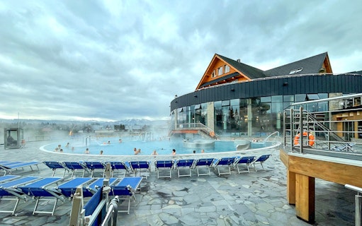 Outdoor pool at Zakopane Thermal Baths with people relaxing, surrounded by mountains.