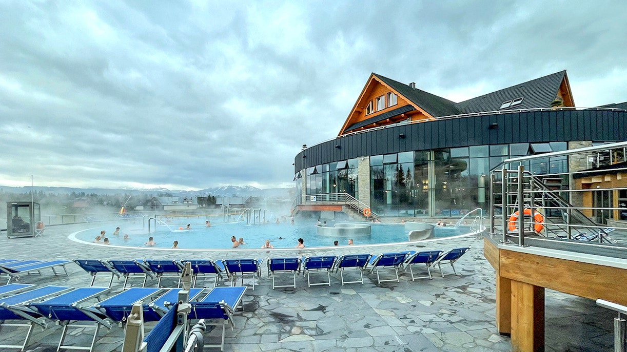 Outdoor pool at Zakopane Thermal Baths with people relaxing, surrounded by mountains.