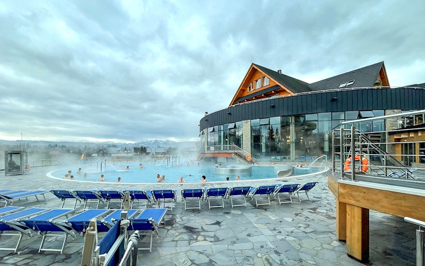 Outdoor pool at Zakopane Thermal Baths with people relaxing, surrounded by mountains.