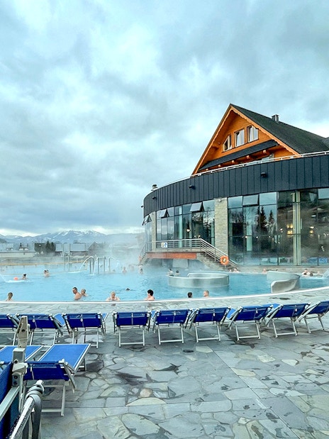 Outdoor pool at Zakopane Thermal Baths with people relaxing, surrounded by mountains.
