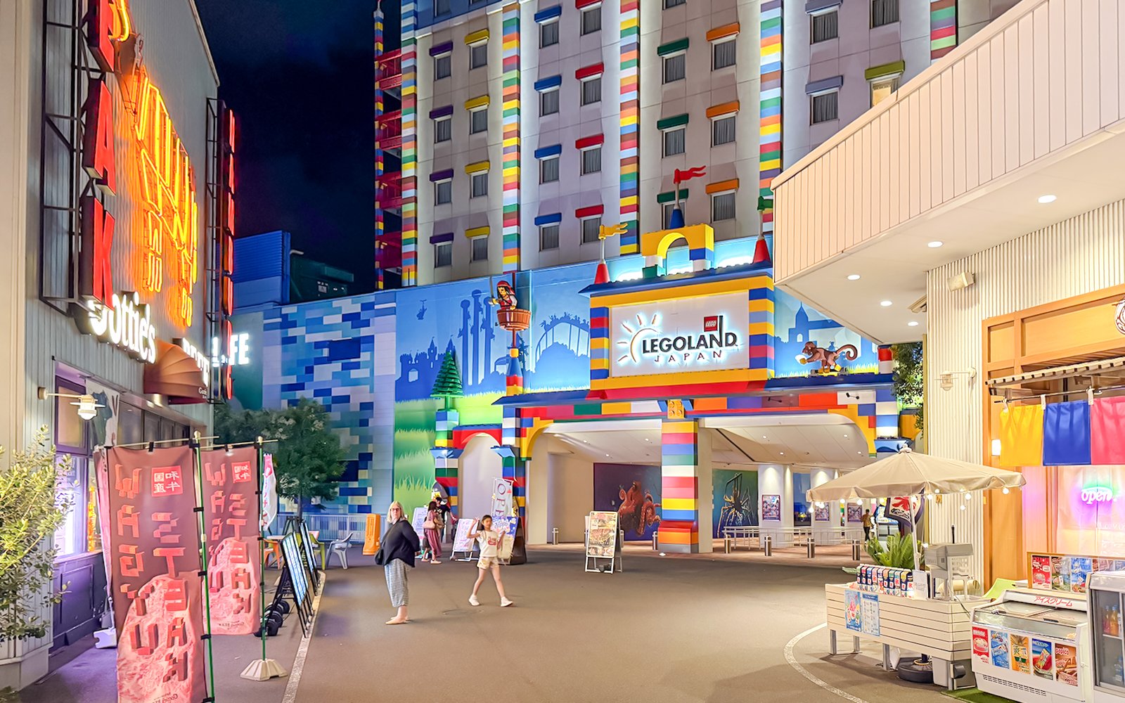 Entrance to Legoland Japan at night with colorful building facade and visitors walking.