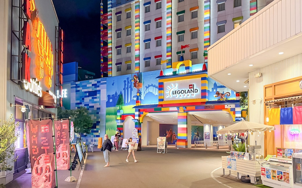 Entrance to Legoland Japan at night with colorful building facade and visitors walking.