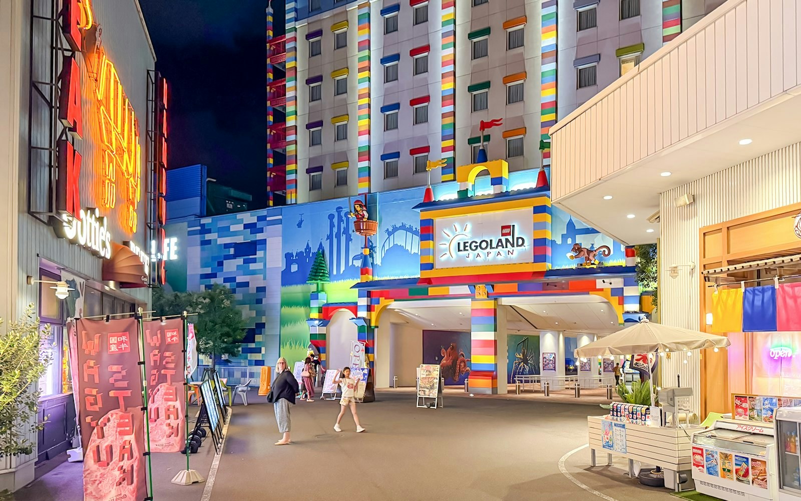 Entrance to Legoland Japan at night with colorful building facade and visitors walking.