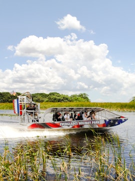 Everglades airboat tour gliding through wetlands under a clear sky.