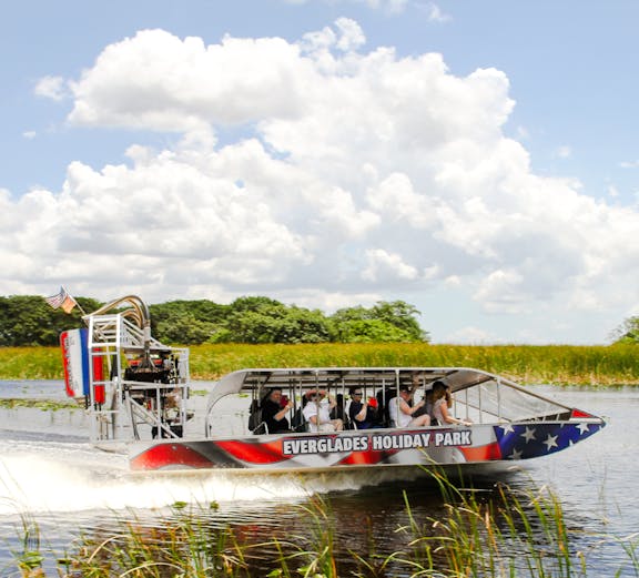 Everglades airboat tour gliding through wetlands under a clear sky.