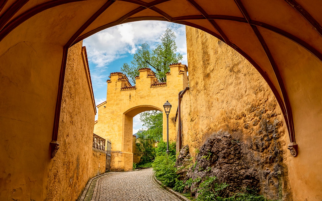 Hohenschwangau Castle archway with cobblestone path and greenery.