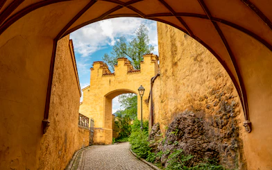 Hohenschwangau Castle archway with cobblestone path and greenery.