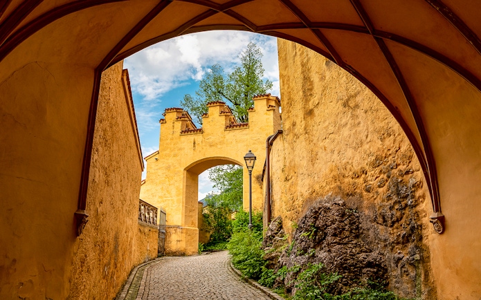 Hohenschwangau Castle archway with cobblestone path and greenery.