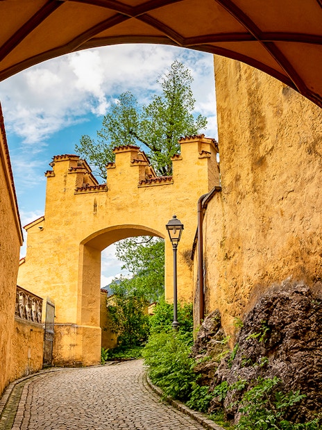 Hohenschwangau Castle archway with cobblestone path and greenery.