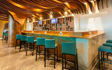 Bar area with teal chairs and wooden ceiling at Primeclass Lounge, Muscat International Airport.