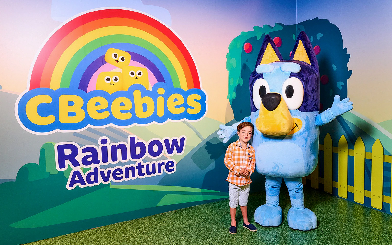 CBeebies Rainbow Adventure sign with child and character mascot.