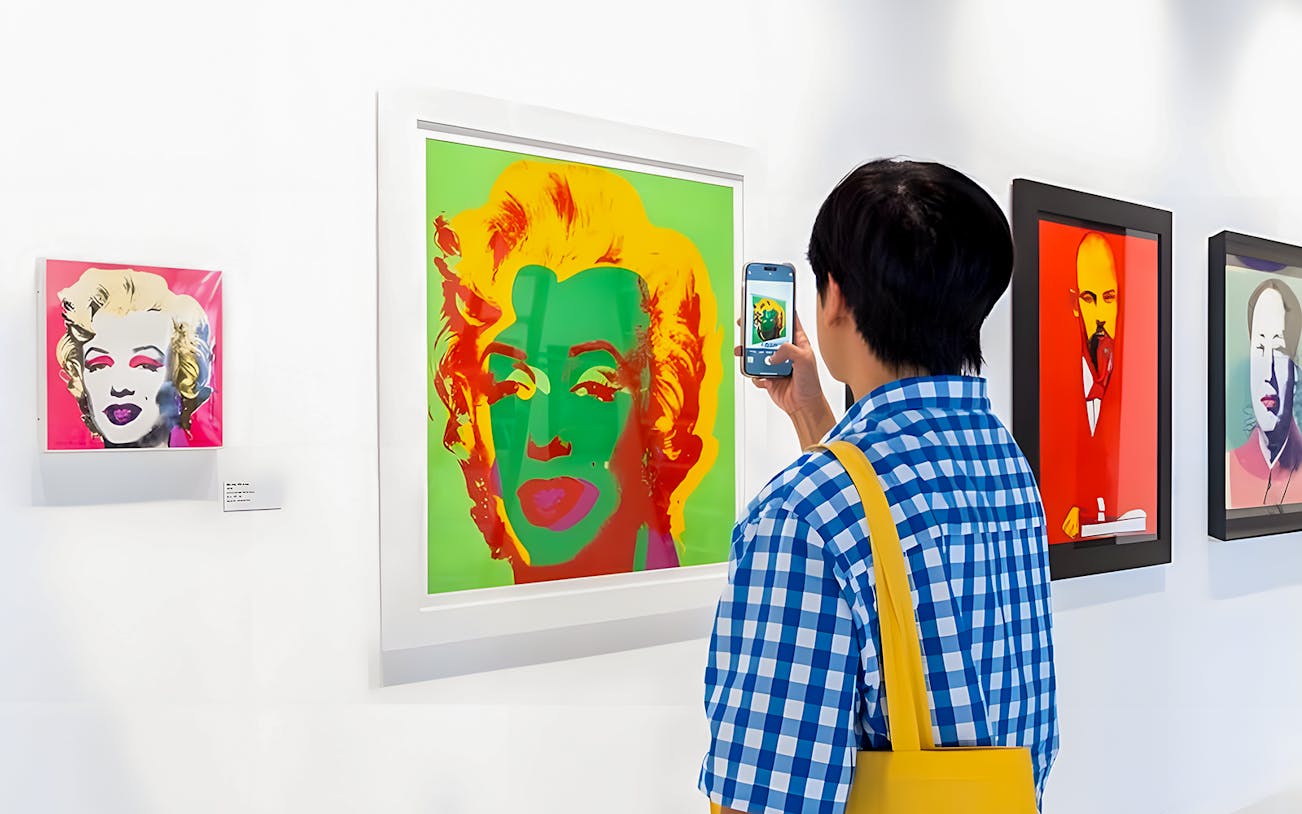 Visitor photographing Andy Warhol's Marilyn Monroe artwork at The Glam Factory exhibit.