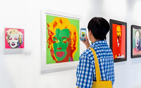 Visitor photographing Andy Warhol's Marilyn Monroe artwork at The Glam Factory exhibit.