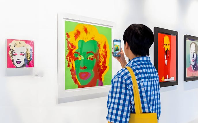 Visitor photographing Andy Warhol's Marilyn Monroe artwork at The Glam Factory exhibit.
