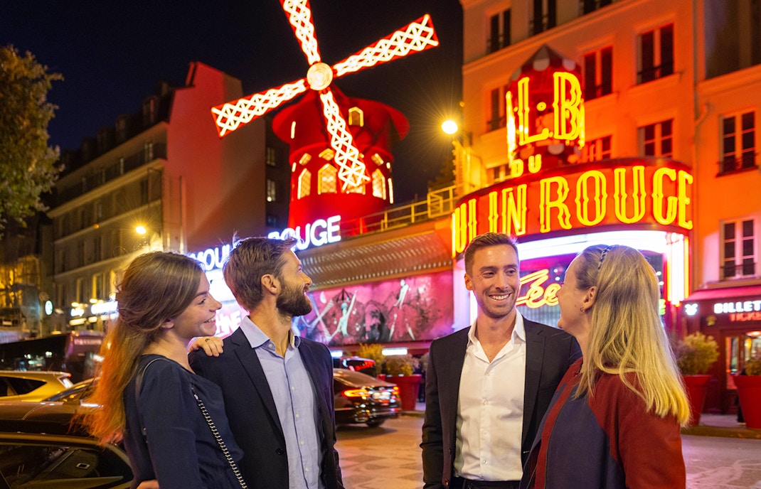 Gruppo fuori dal Moulin Rouge a Parigi di notte con l'iconico mulino a vento.