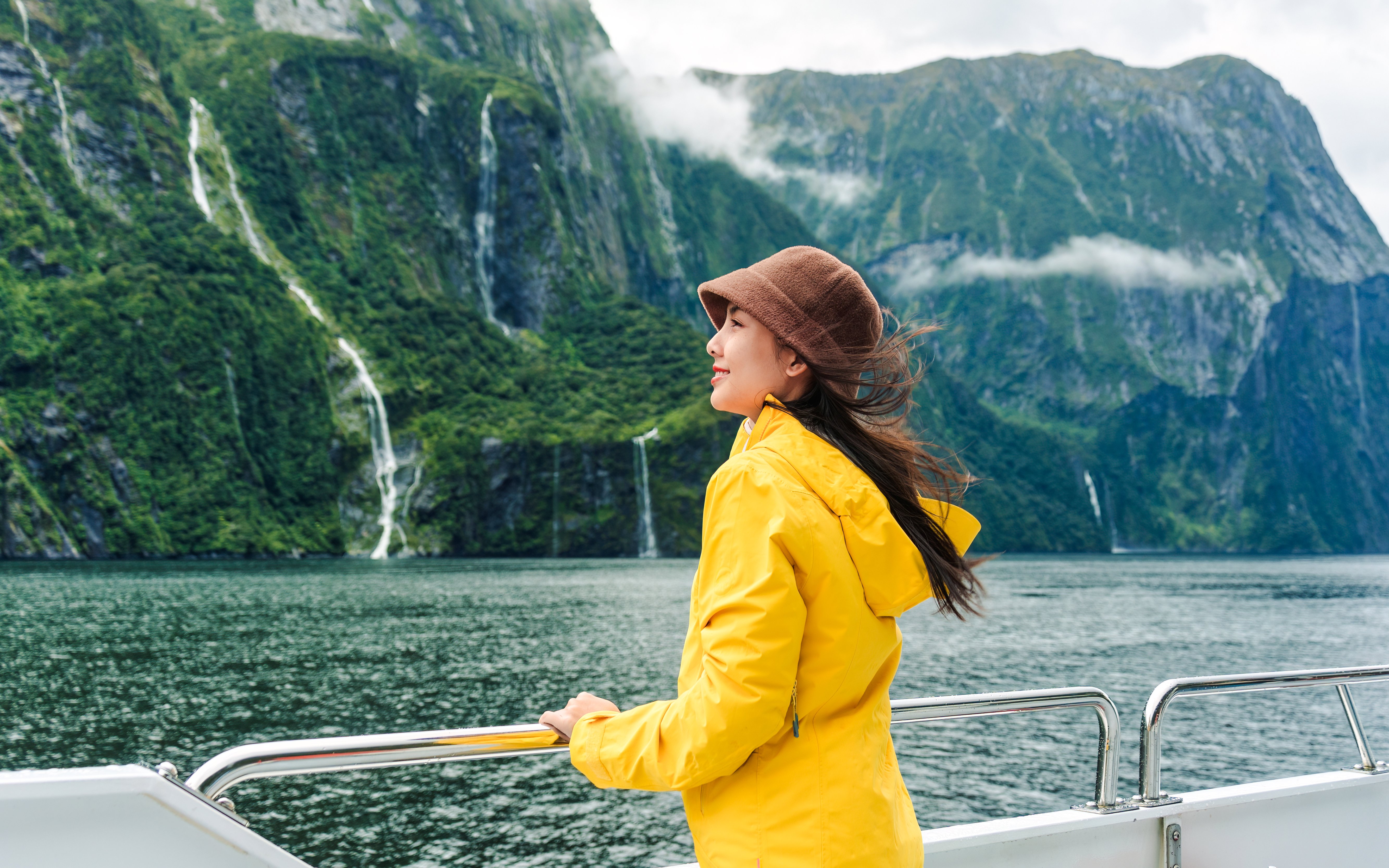 Asian woman on ferry enjoying Milford Sound view, New Zealand.