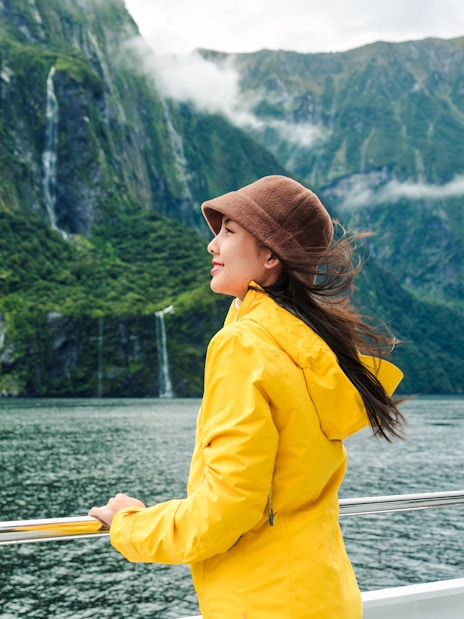 Asian woman on ferry enjoying Milford Sound view, New Zealand.