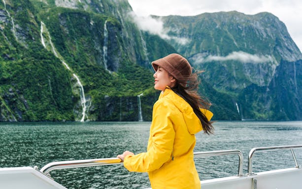 Asian woman on ferry enjoying Milford Sound view, New Zealand.