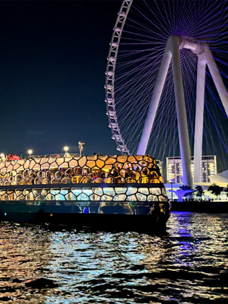 Dinner cruise boat on Dubai waters with illuminated Ferris wheel in the background.