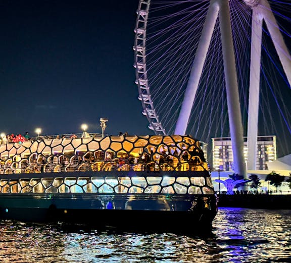 Dinner cruise boat on Dubai waters with illuminated Ferris wheel in the background.