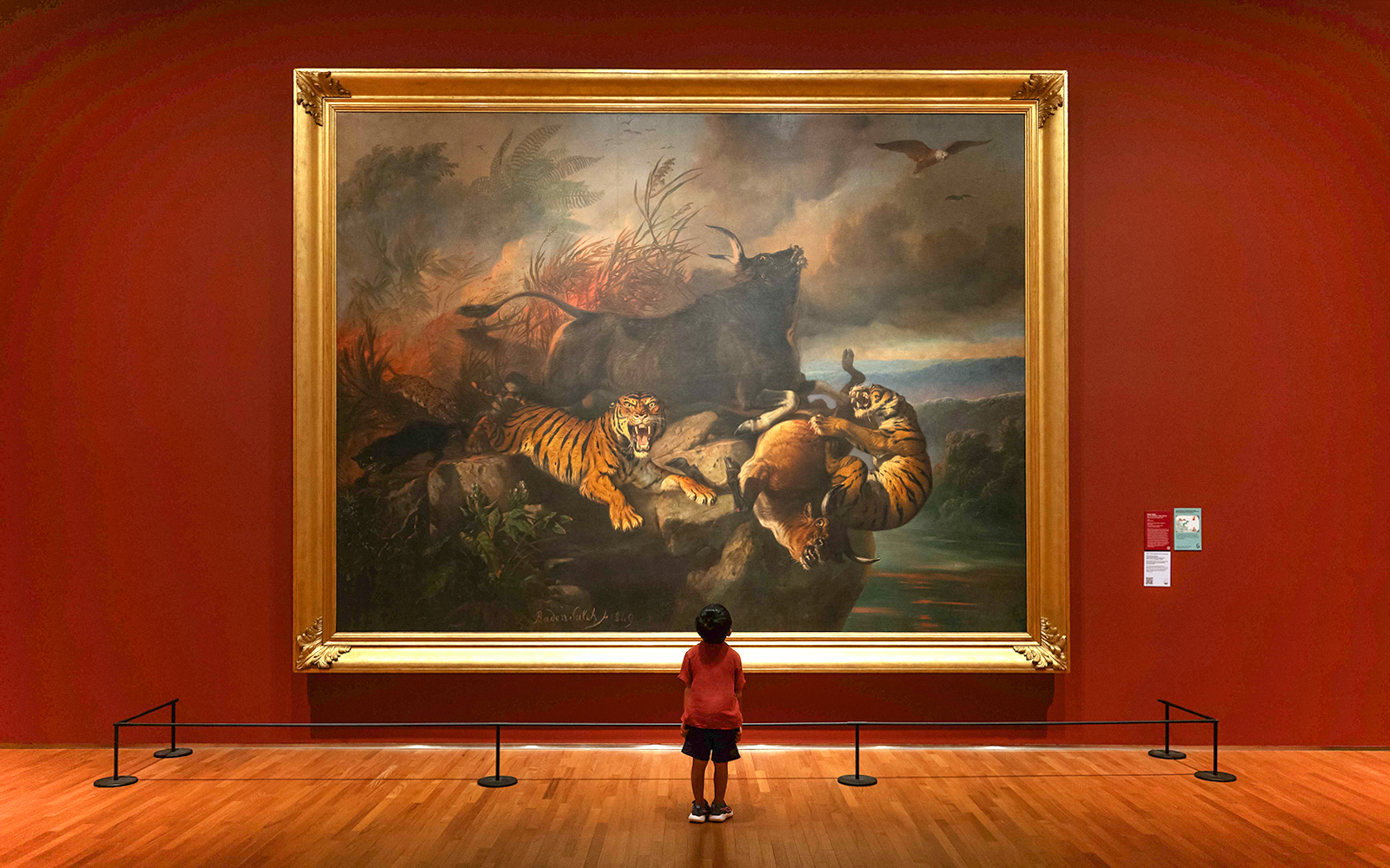 Child viewing a large painting of tigers and wildlife at National Gallery Singapore.