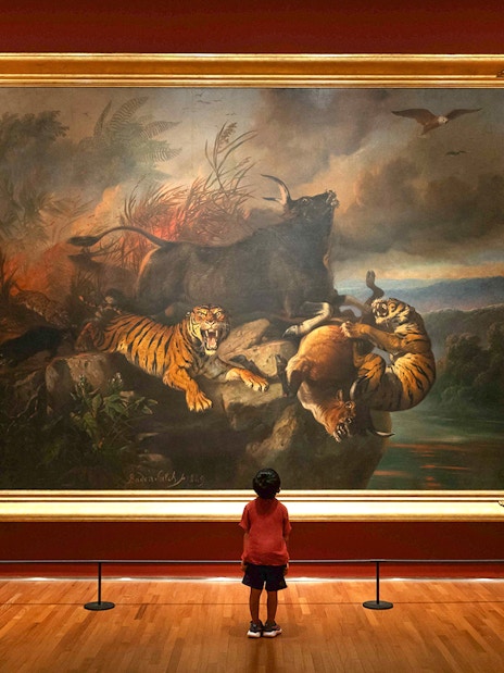 Child viewing a large painting of tigers and wildlife at National Gallery Singapore.
