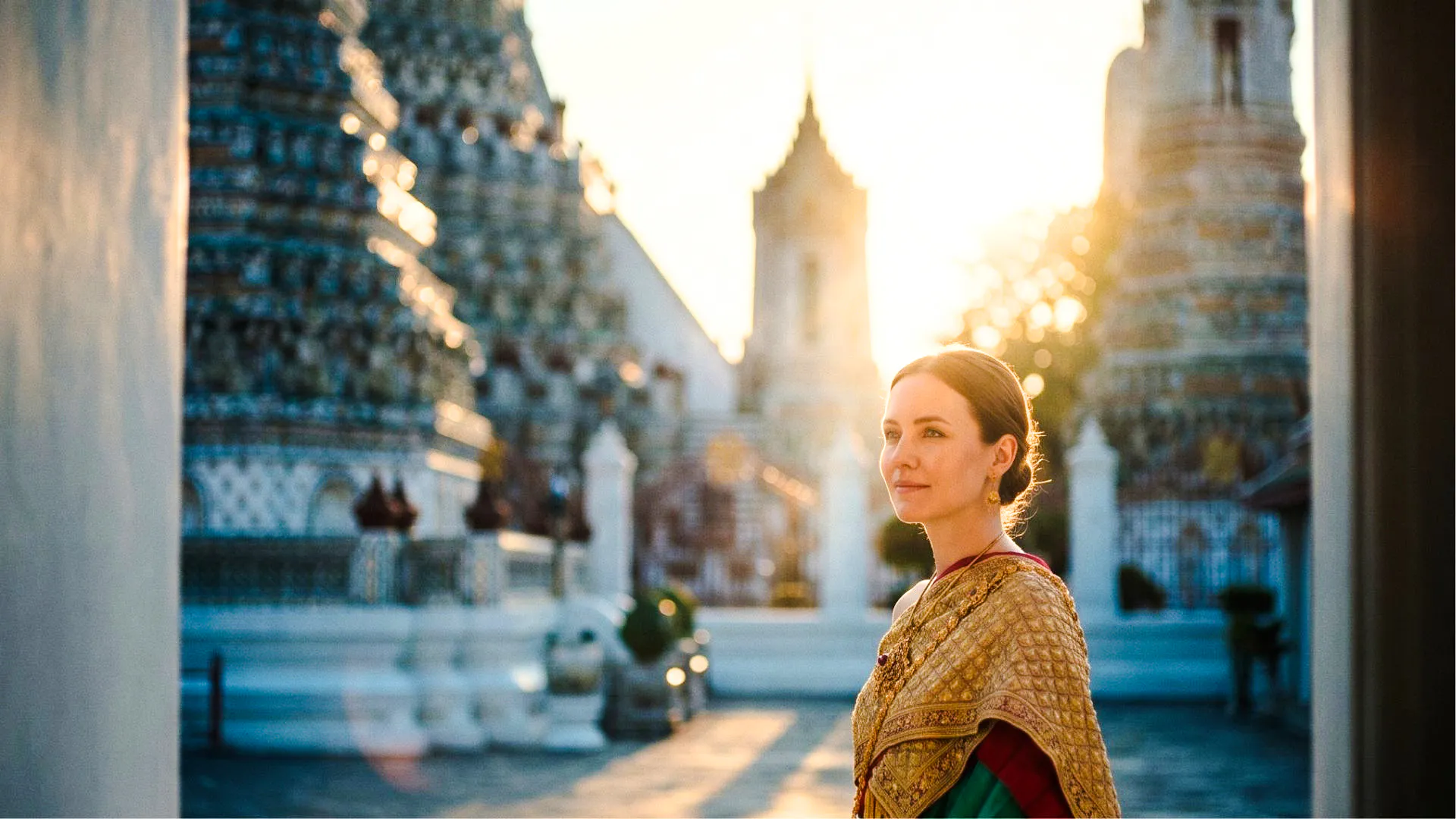 Tourist in traditional Thai costume at Wat Arun, Bangkok, with temple spires in the background.