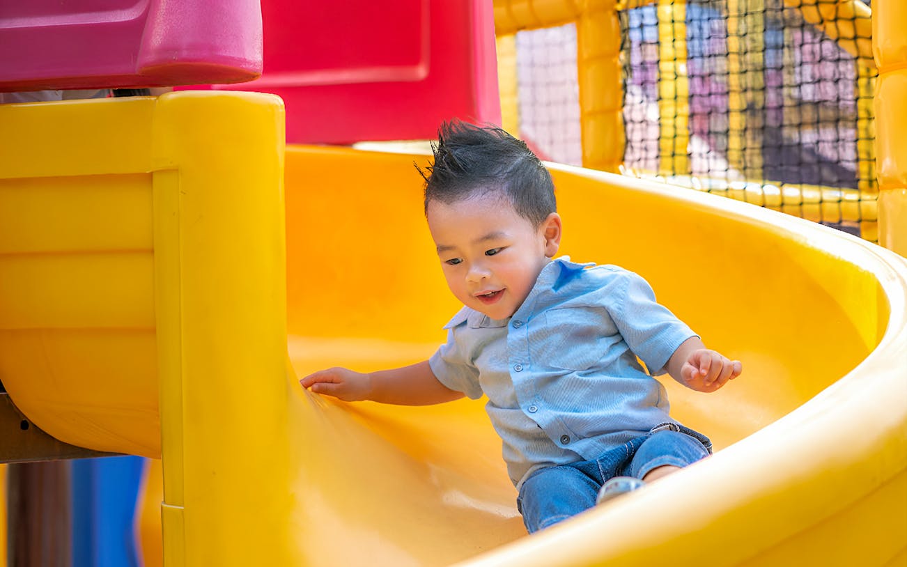 Child sliding down a yellow slide at Wonderpark Melaka.