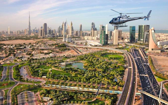 Helicopter flying over Dubai cityscape with Burj Khalifa in view.