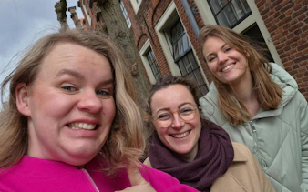 Three people smiling in front of historic brick buildings in Haarlem during a self-guided city exploration game.