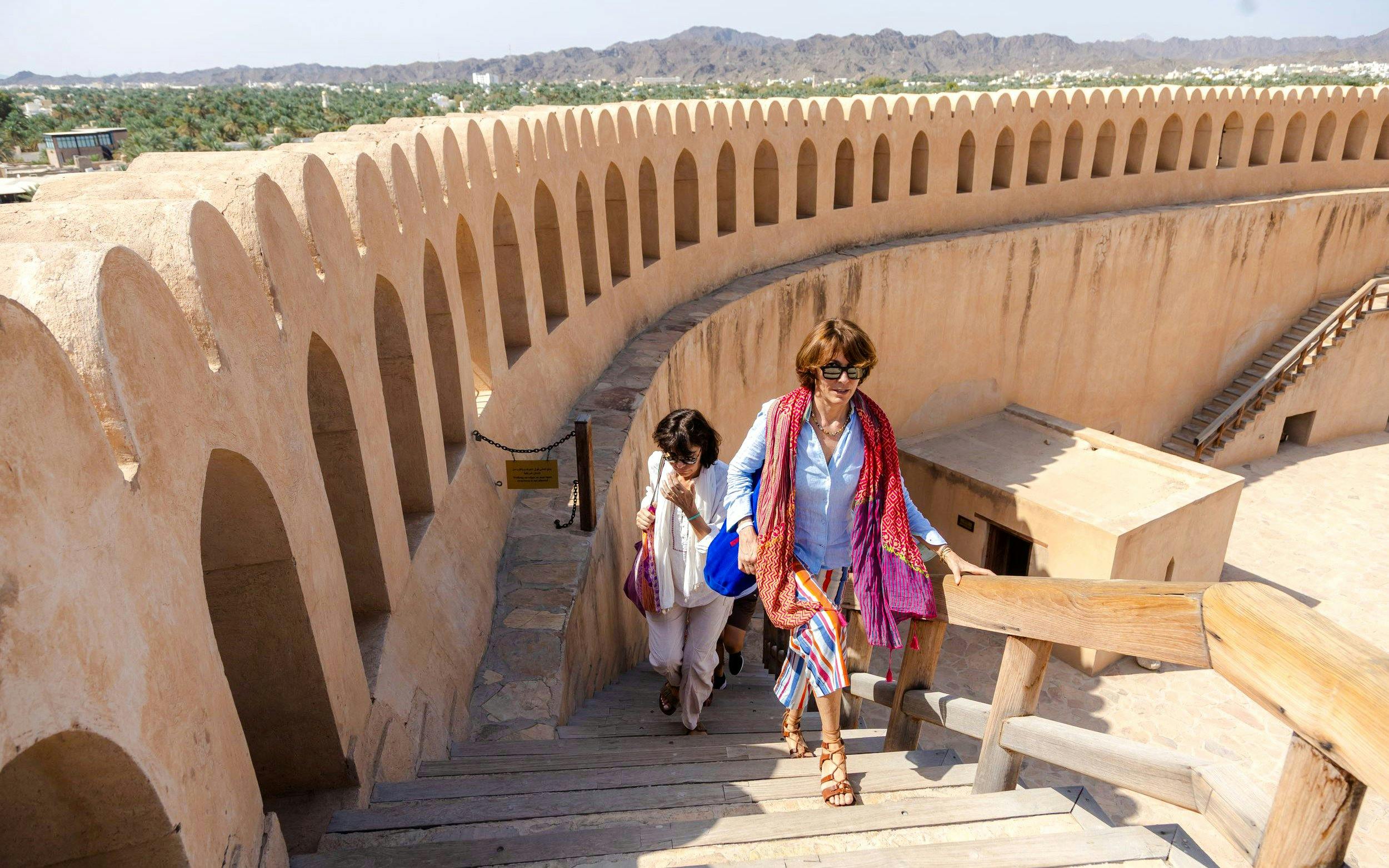 Visitors ascending stairs at Nizwa Fort, Oman, with mountain views in the background.