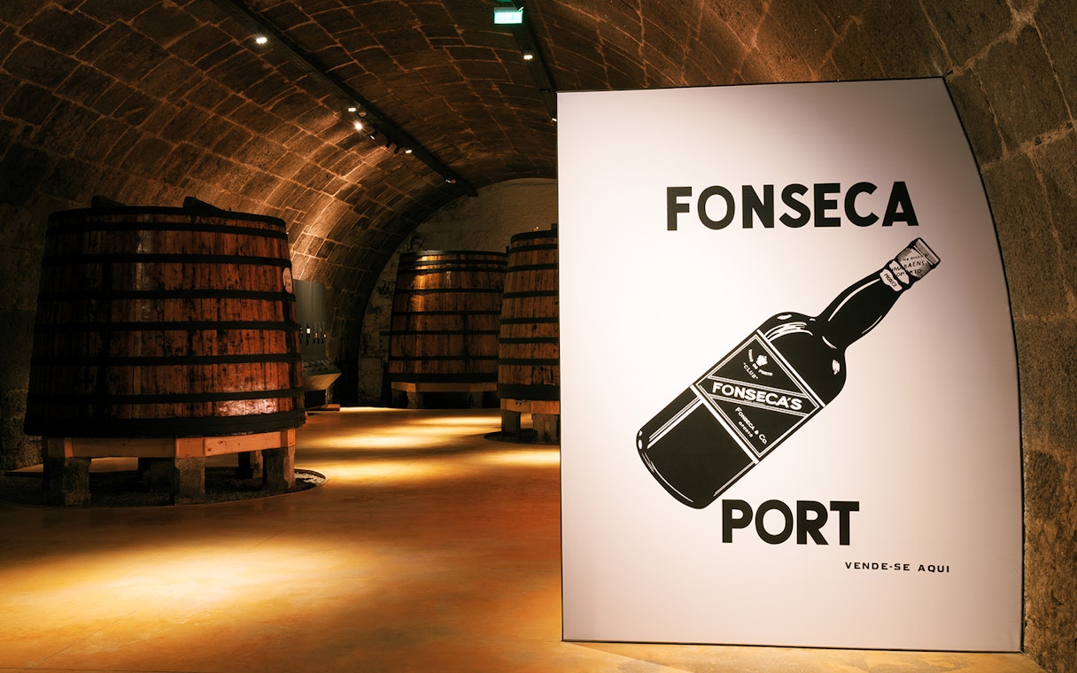 Fonseca port wine cellar with large wooden barrels in dimly lit stone archway.