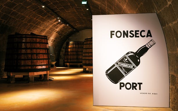 Fonseca port wine cellar with large wooden barrels in dimly lit stone archway.