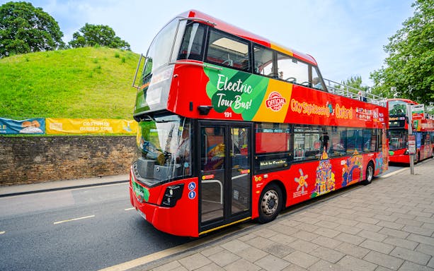 Oxford sightseeing bus passing historic building.