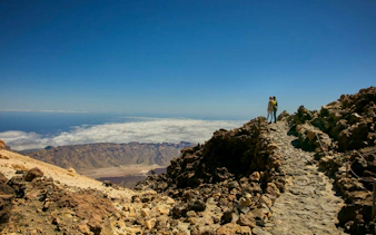 Guests on Mount Teide summit path with views of volcanic landscape and clouds.