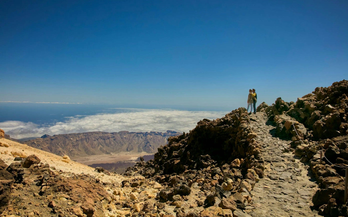 Guests on Mount Teide summit path with views of volcanic landscape and clouds.