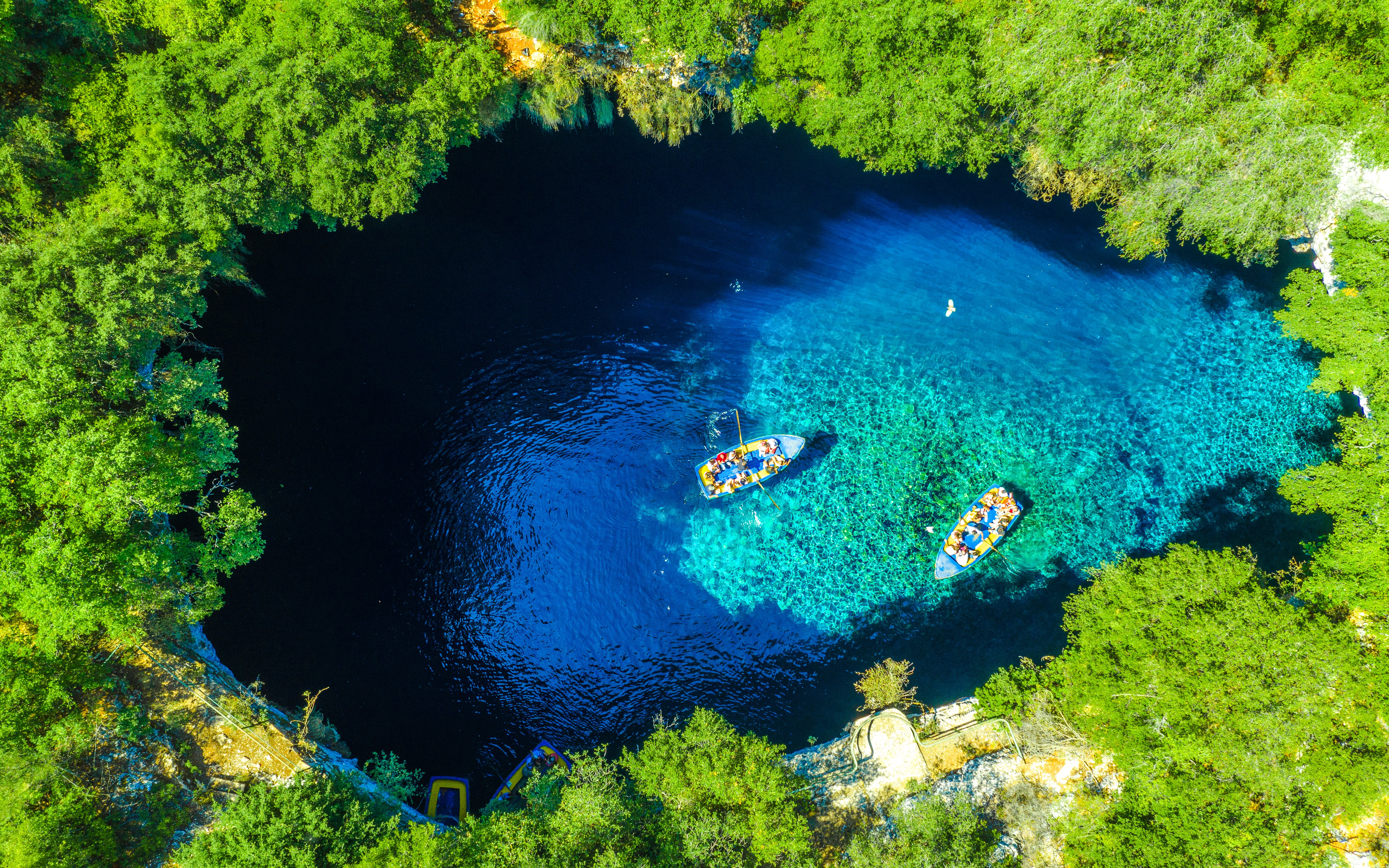 Boats on Melissani Lake surrounded by lush greenery on Kefalonia Island, Greece.