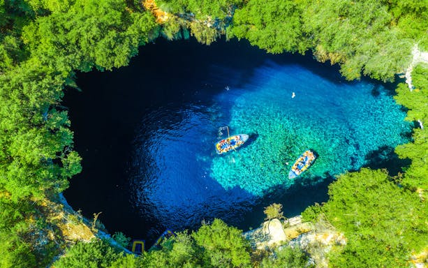 Boats on Melissani Lake surrounded by lush greenery on Kefalonia Island, Greece.