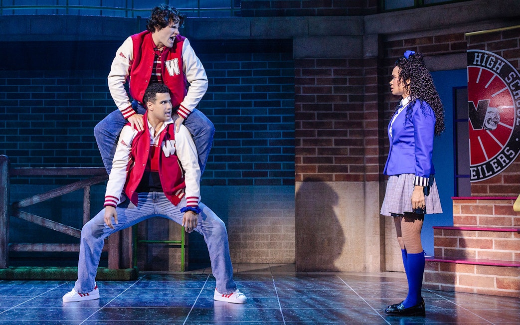 Two actors in red jackets perform a scene from Heathers: The Musical on stage.