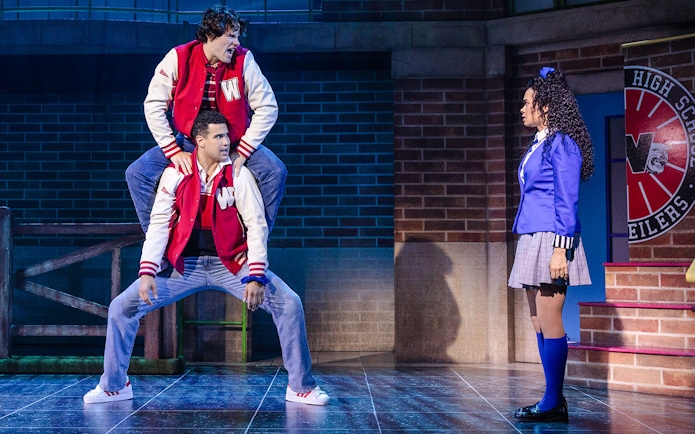 Two actors in red jackets perform a scene from Heathers: The Musical on stage.