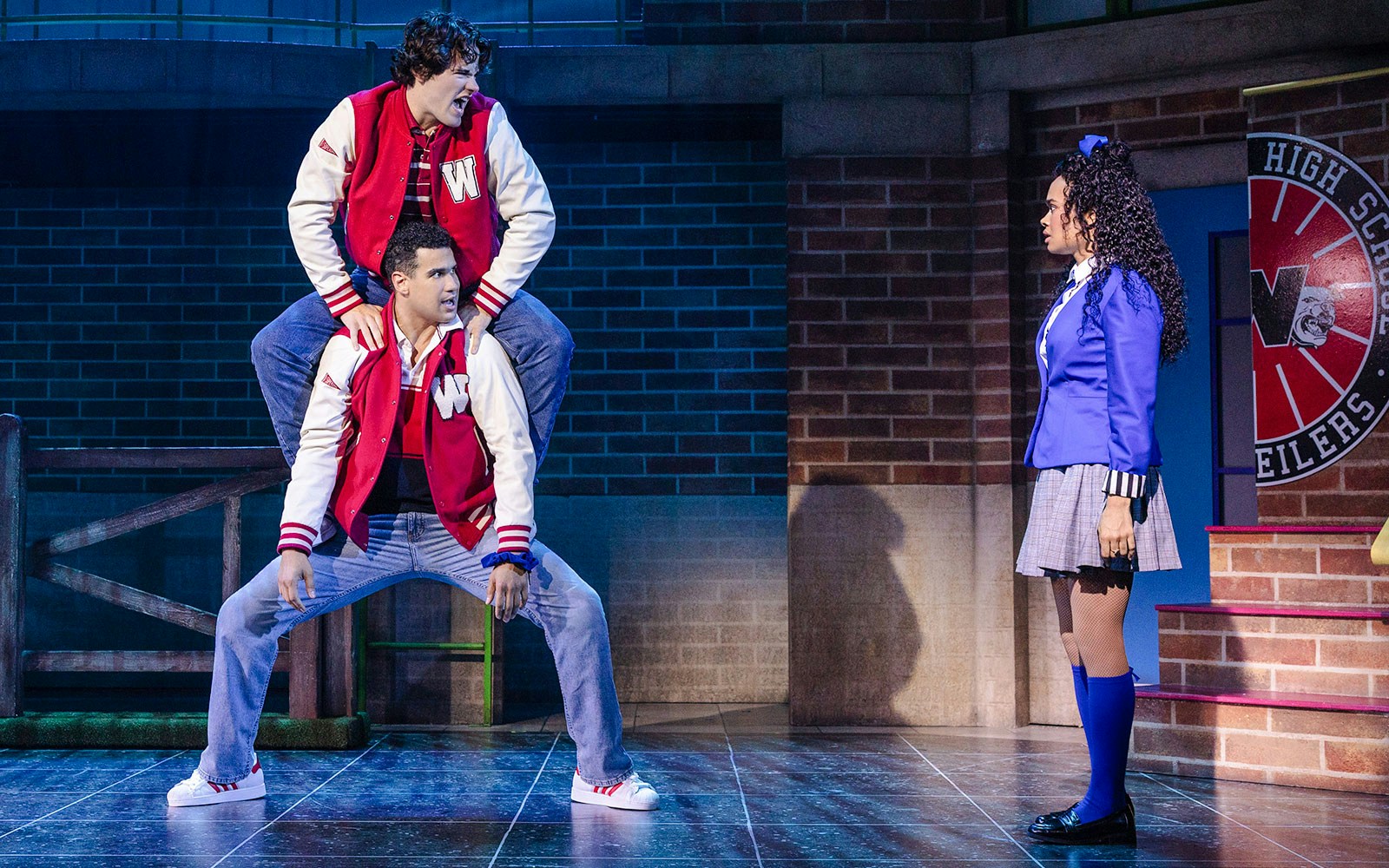 Two actors in red jackets perform a scene from Heathers: The Musical on stage.