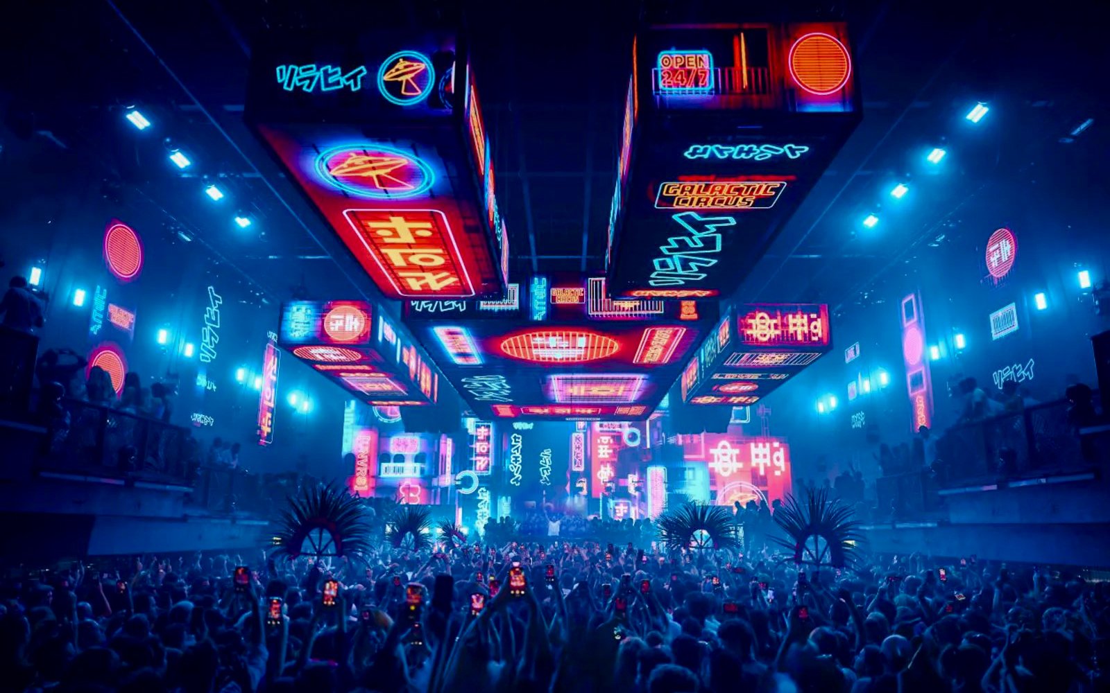 Crowd at UNVRS David Guetta Galactic Circus in Ibiza with neon lights and vibrant displays.
