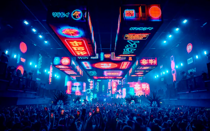 Crowd at UNVRS David Guetta Galactic Circus in Ibiza with neon lights and vibrant displays.