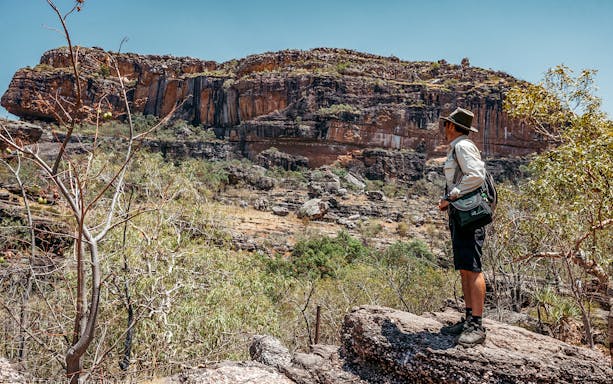 Person hiking in Kakadu National Park, Australia, viewing rocky escarpments and bushland.
