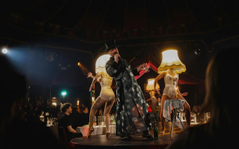 Performer in top hat at Burlesque Dinner Club, Vienna with dancers on stage.