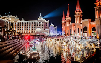 Boat parade at Land of Legends Night Show with illuminated buildings and crowd.