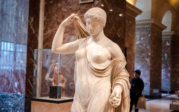 Tourists viewing a classical statue inside the Louvre Museum, France.