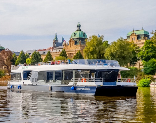 Sightseeing boat on Vltava River with historic Prague architecture in the background.