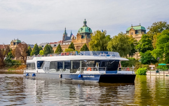 Sightseeing boat on Vltava River with historic Prague architecture in the background.