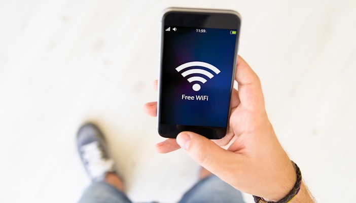 Man holding smartphone displaying free WiFi icon.